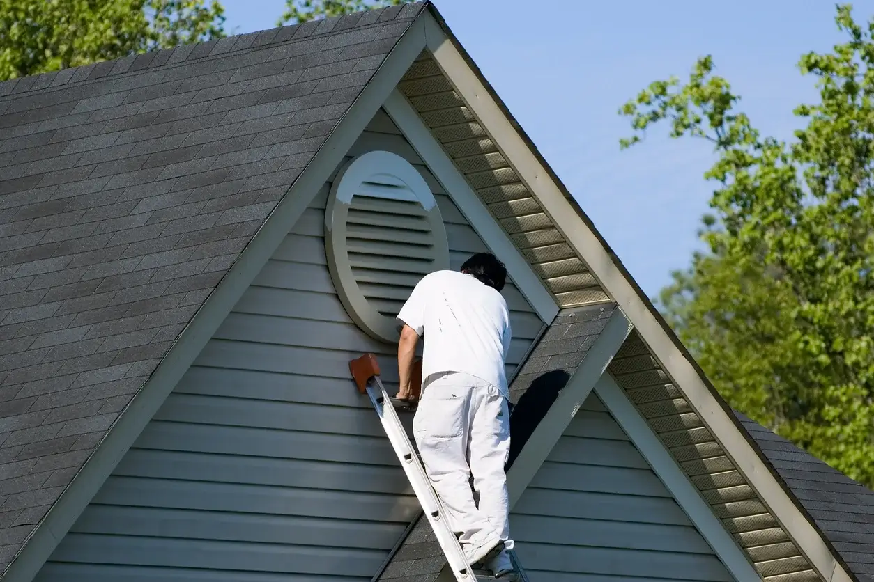 A painter on a ladder painting the siding of a house