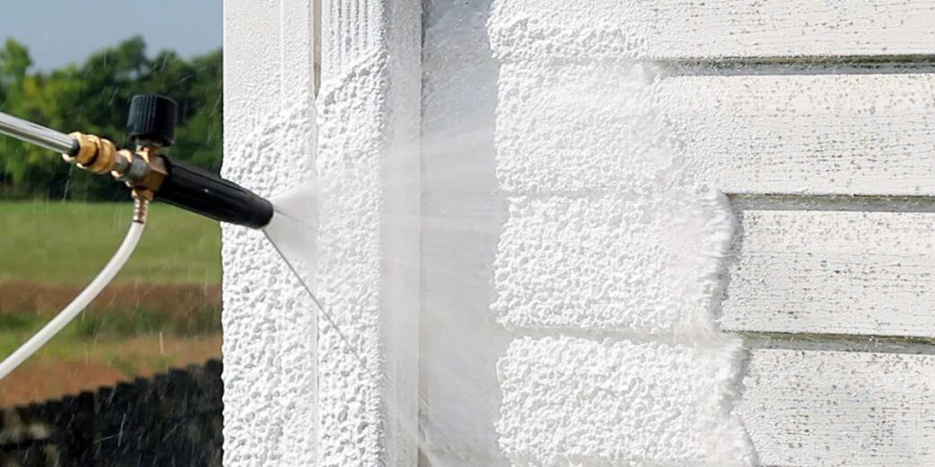 A professional power washing the exterior of a house
